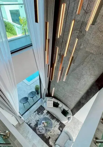 Luxurious modern living room with high ceilings and elegant lighting, overlooking a serene outdoor pool area.