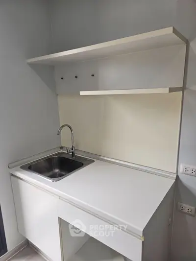 Modern minimalist kitchen with sleek white cabinetry and stainless steel sink, perfect for compact spaces.