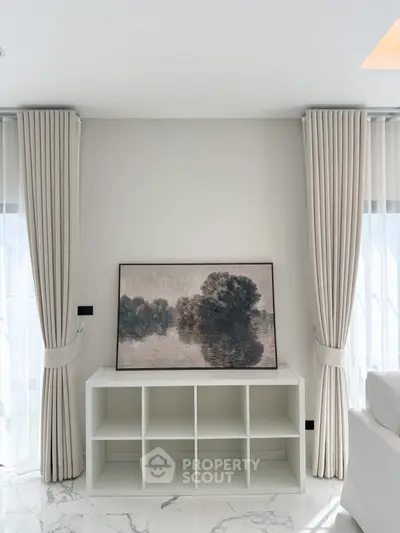 Elegant living room with modern decor and natural light, featuring stylish curtains and a framed landscape painting.
