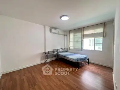 Spacious bedroom with wooden flooring and natural light, featuring a bed and desk.