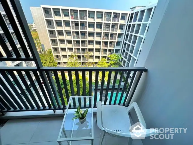 Cozy balcony with modern furniture overlooking a serene pool and lush greenery, perfect for relaxing outdoor moments in a contemporary urban residence.