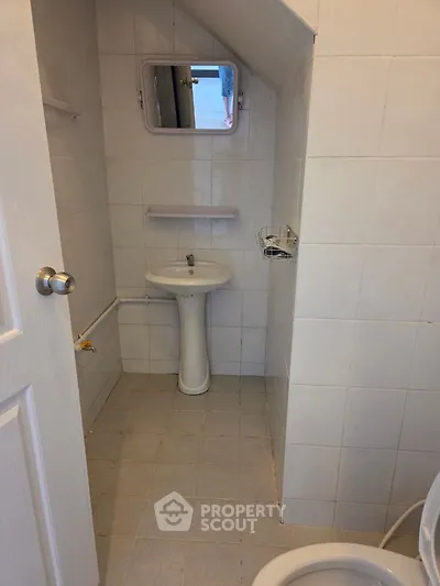 Compact bathroom with pedestal sink and wall-mounted mirror in a tiled space.