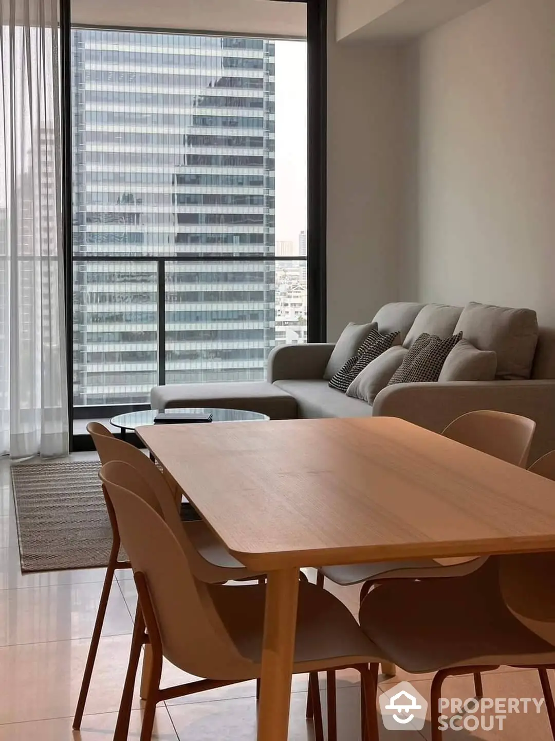 Chic modern living room with floor-to-ceiling windows offering an urban view, complemented by a stylish wooden dining set and cozy sofa.