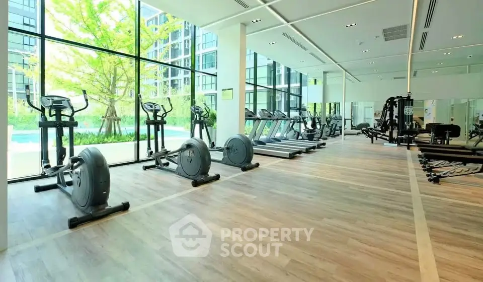 Spacious modern gym with large windows and state-of-the-art equipment in luxury building.