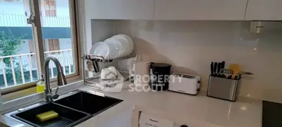 Modern kitchen with sleek white countertops, built-in appliances, and a view of the balcony.