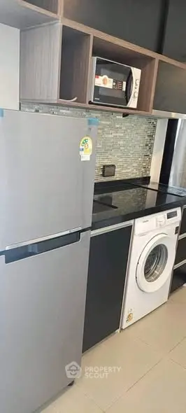 Modern kitchen with fridge, microwave, and washing machine in sleek design.