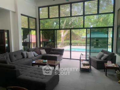 Spacious living room with large windows overlooking a pool and lush greenery, featuring modern gray sofas.