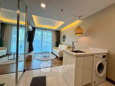 Modern living room with open kitchen and washing machine, featuring stylish decor and natural light.