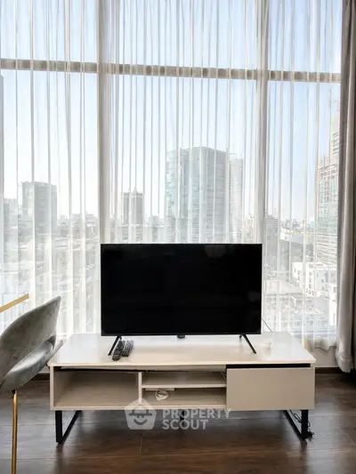 Modern living room with large windows offering stunning city views, featuring sleek TV setup and elegant decor.