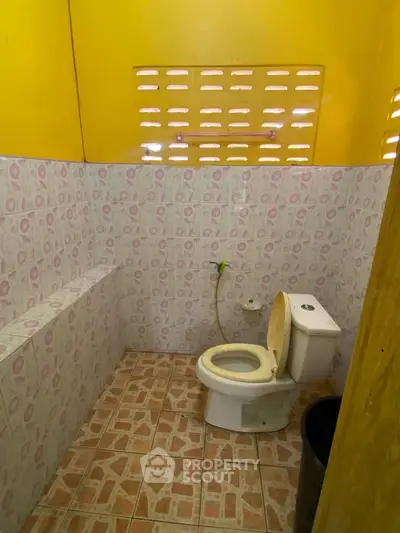 Cozy bathroom with vibrant yellow walls and patterned tiles, featuring a standard toilet and natural light.