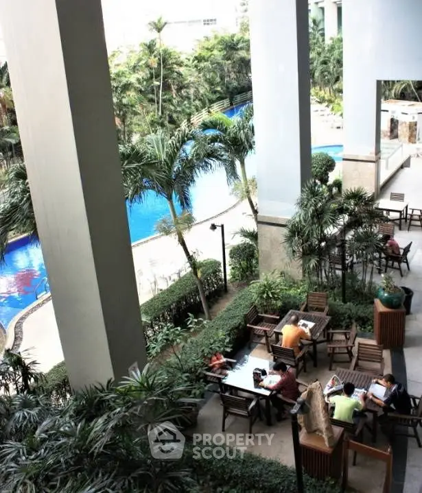 Luxurious poolside view with lush greenery and outdoor seating area in modern residential complex.