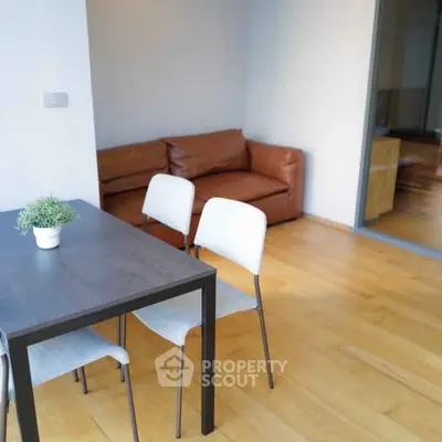 Modern living room with wooden flooring, cozy brown sofa, and sleek dining table with chairs.