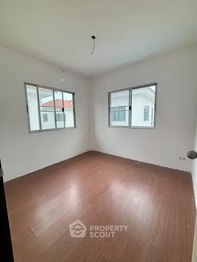 Spacious empty bedroom with wooden flooring and large windows in modern home.