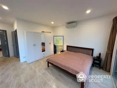 Spacious bedroom with polished tile flooring, large white wardrobe, and a wooden bed frame, exuding a serene and comfortable ambiance.