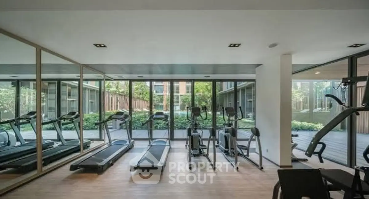 Modern gym with treadmills and exercise equipment overlooking lush garden view.