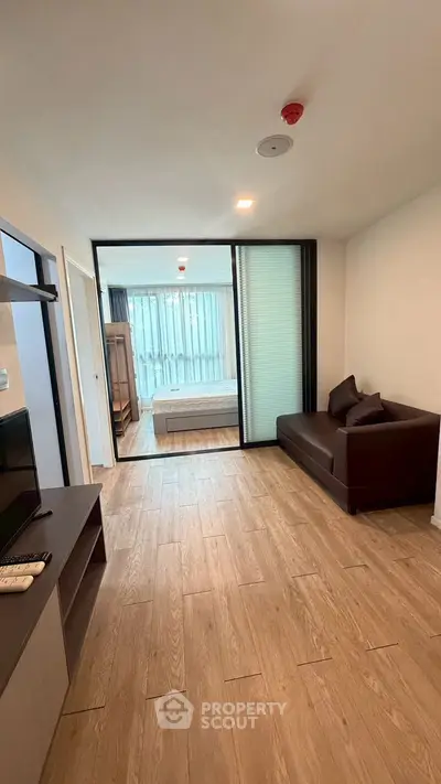 Modern apartment with open living room and bedroom, featuring sleek wooden flooring and contemporary furnishings.