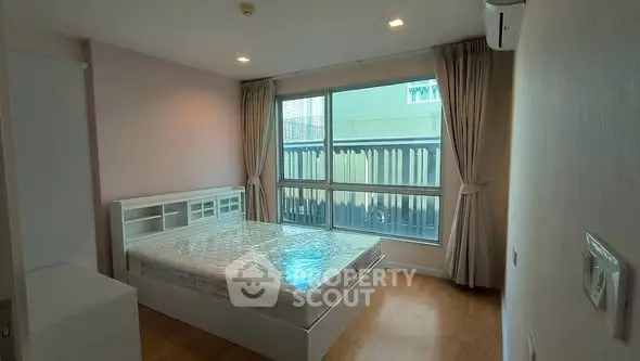 Spacious bedroom with large window and natural light in modern apartment.