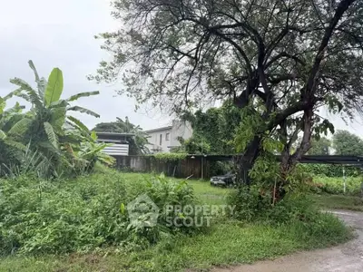 Lush green garden with mature trees and a view of a residential building in the background.
