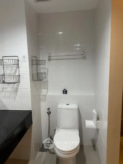 Modern bathroom with sleek black countertop and white tiled walls, featuring a toilet and wall-mounted storage racks.