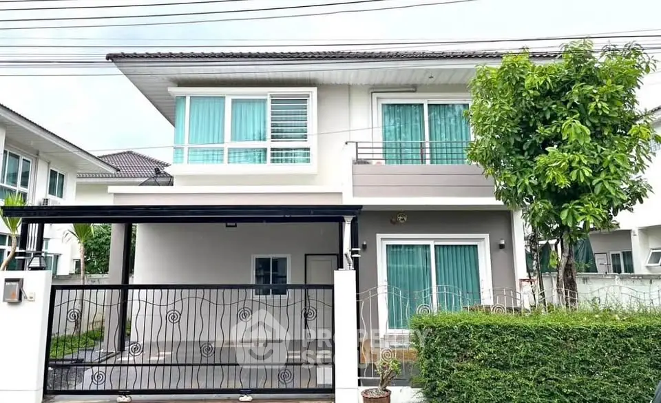 Modern two-story house with balcony and lush greenery in a serene neighborhood.