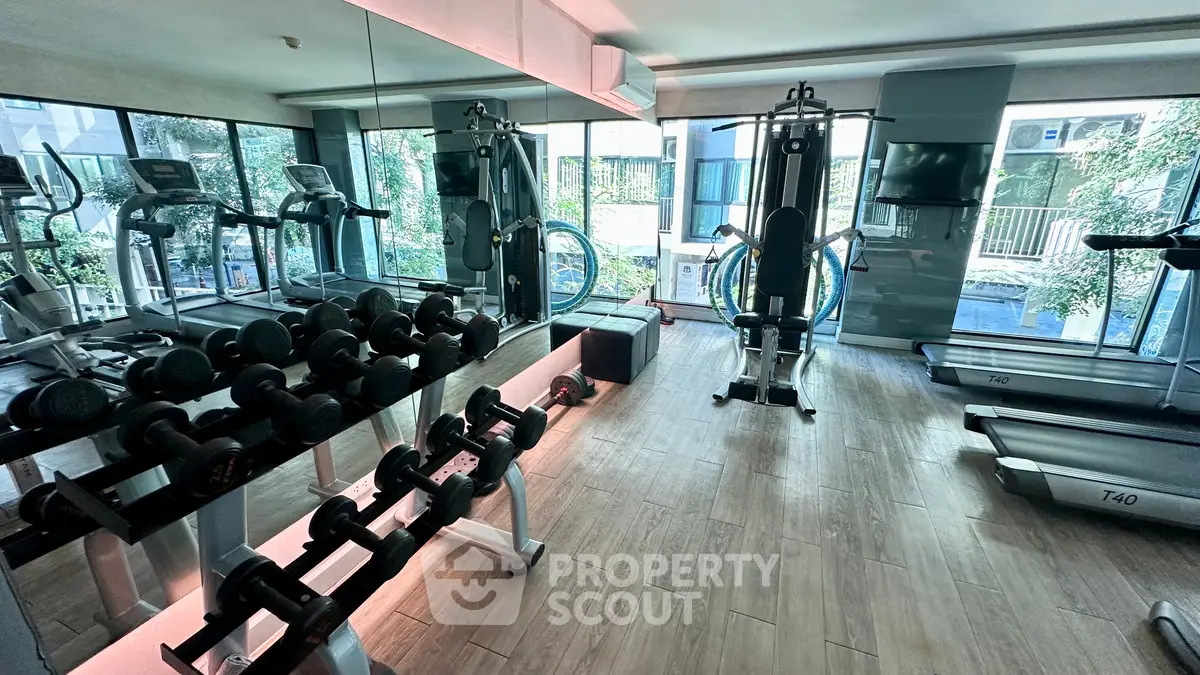 Modern gym with state-of-the-art equipment and floor-to-ceiling windows in luxury apartment complex.