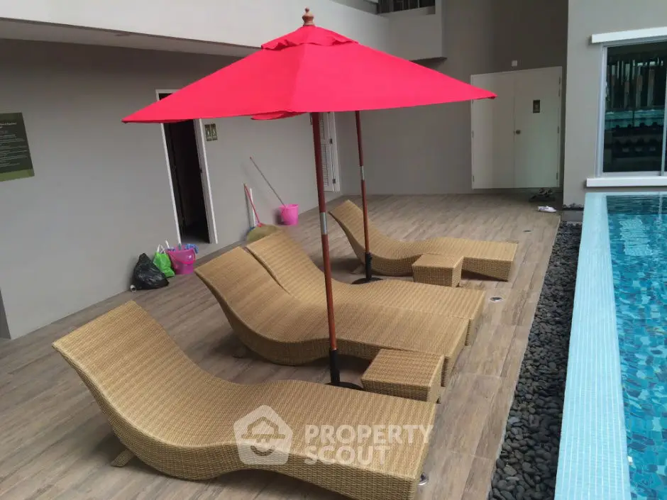 Luxurious poolside area with stylish loungers and vibrant red umbrella, perfect for relaxation and leisure.