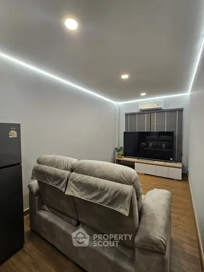Modern living room with cozy sofa and large TV, featuring sleek lighting and wooden flooring.