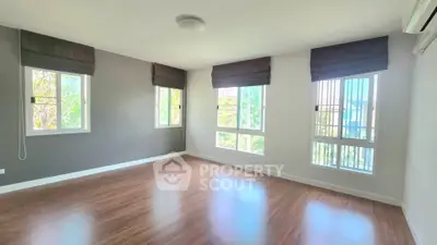 Spacious sunlit room with large windows and wooden flooring, perfect for a cozy living space.