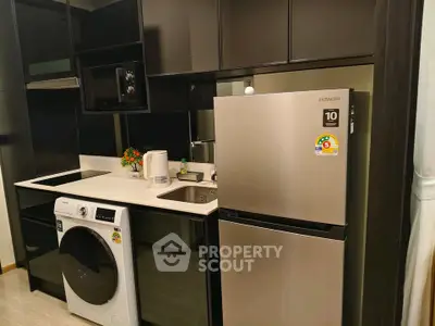 Modern kitchen with sleek black cabinets, stainless steel fridge, and washing machine.