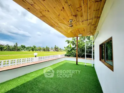 Spacious balcony with lush green artificial grass and wooden ceiling, offering serene views of the countryside.