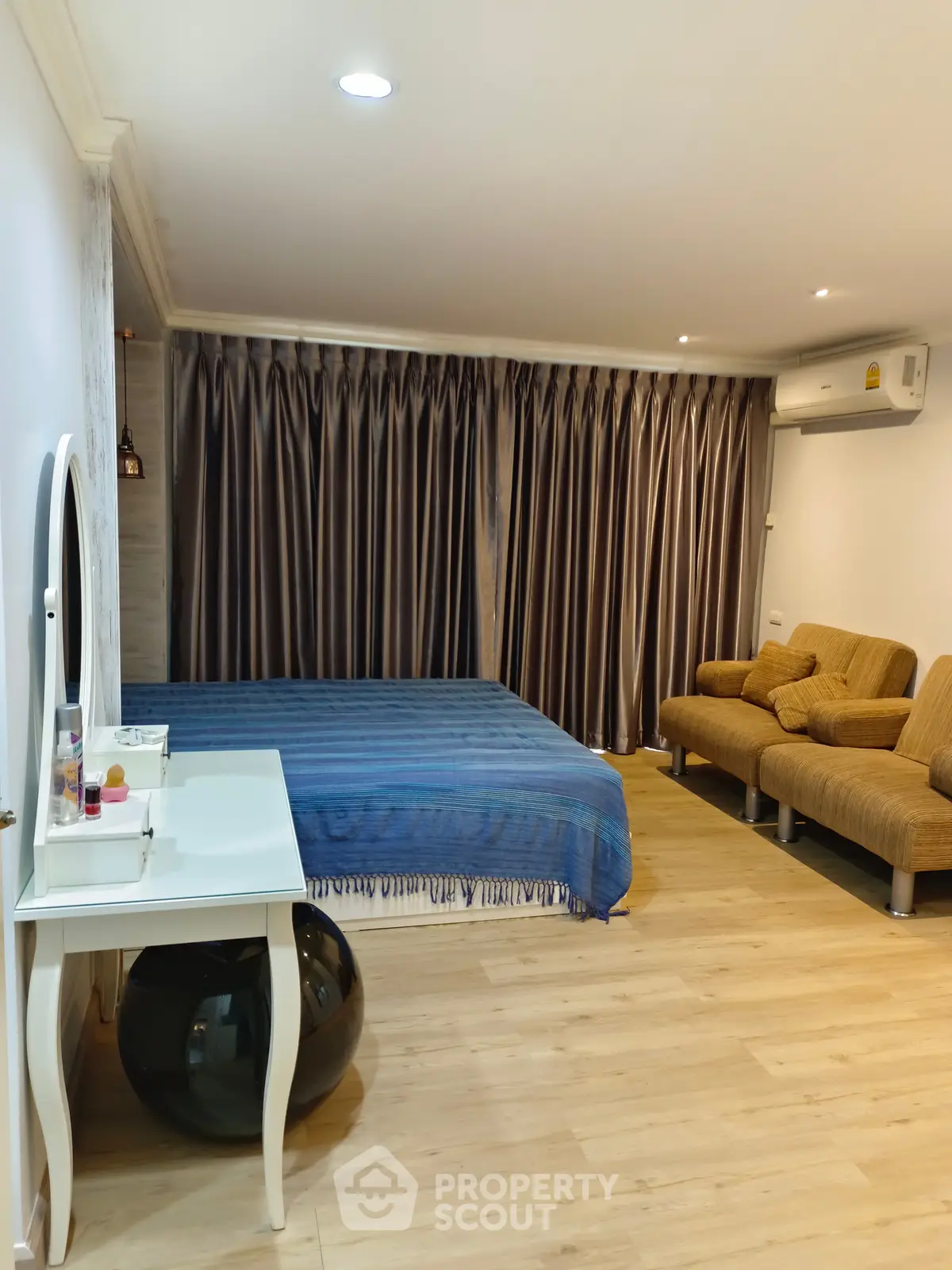 Spacious bedroom with modern decor and cozy seating area, featuring elegant curtains and wooden flooring.