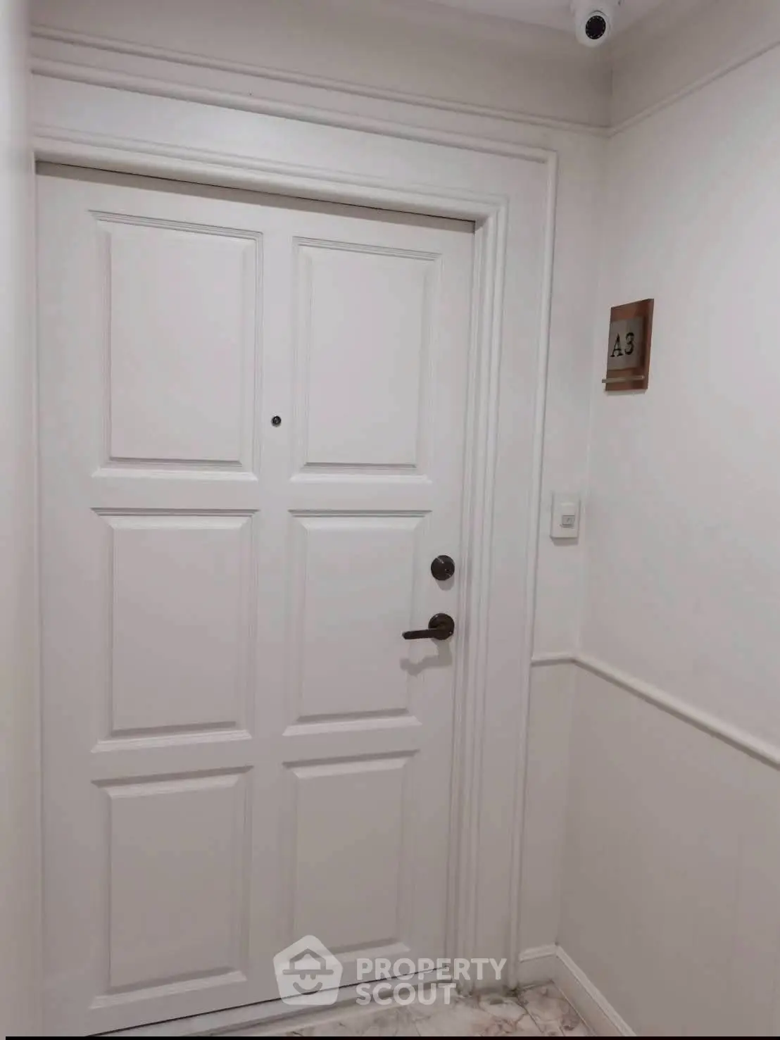 Elegant white apartment entrance with security camera and unit number A3.