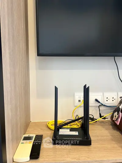 Modern living space with TV, router, and remote controls on a wooden shelf.