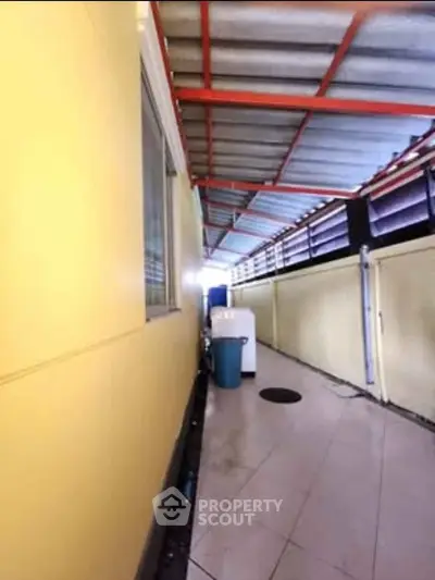 Covered outdoor corridor with washing machine and yellow walls