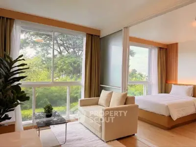 Spacious bedroom with large windows and lush garden view, featuring cozy seating area and modern decor.