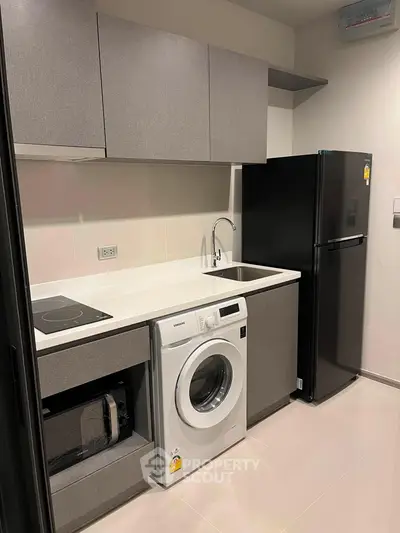 Modern kitchen with sleek cabinetry, washing machine, and black refrigerator in a compact layout.
