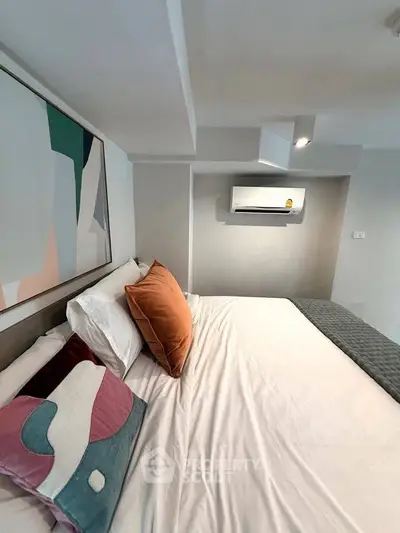 Modern bedroom with stylish decor and air conditioning unit, featuring abstract art and cozy bedding.