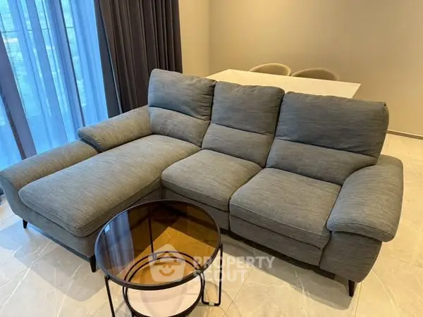 Modern living room with stylish gray sofa and round glass coffee table