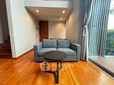 Modern living room with wooden flooring and large windows overlooking a pool, featuring a cozy sofa and stylish coffee table.