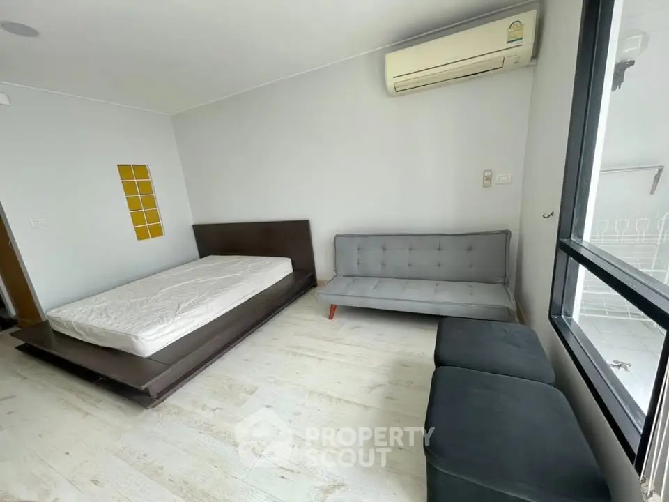 Modern bedroom with minimalist design, featuring a bed, sofa, and air conditioning.