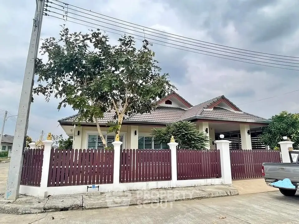 Charming single-story house with fenced yard and lush greenery under a cloudy sky.