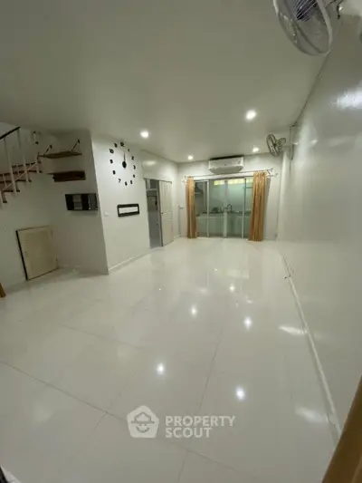 Spacious and bright living area with glossy white tiles, modern lighting, and a staircase leading to an upper level, perfect for family gatherings.