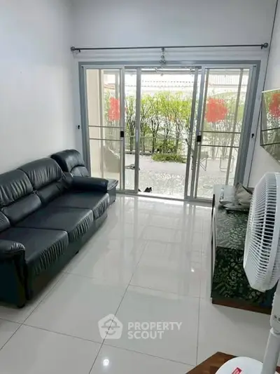 Spacious living room with sleek leather sofa and large sliding glass doors opening to a lush garden view.