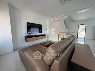 Modern living room with sleek leather sofa and wall-mounted TV, featuring minimalist design and natural light.