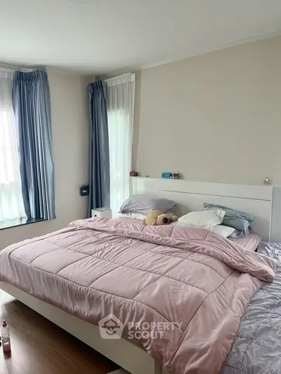 Cozy bedroom with large windows and soft pink bedding, perfect for relaxation.