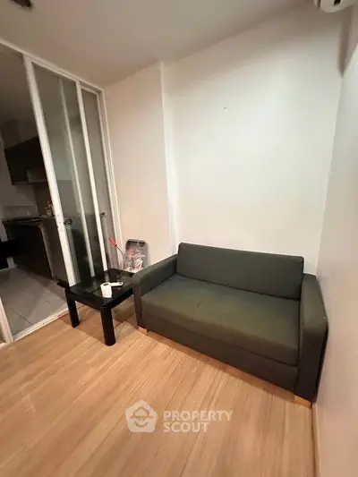 Cozy living room with compact sofa and sliding glass doors leading to kitchen area.