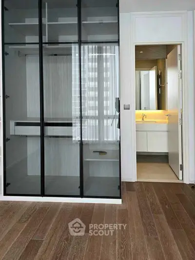 Modern interior with glass closet and bathroom view, featuring sleek design and wooden flooring.