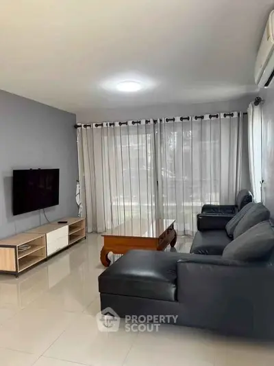 Spacious living room with modern black leather sofas and large TV, perfect for relaxation.