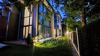 Stunning modern home exterior with large windows and lush garden at twilight.