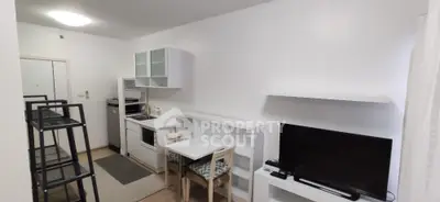 Modern compact living room with integrated kitchen and dining area, featuring sleek white furniture and a flat-screen TV.